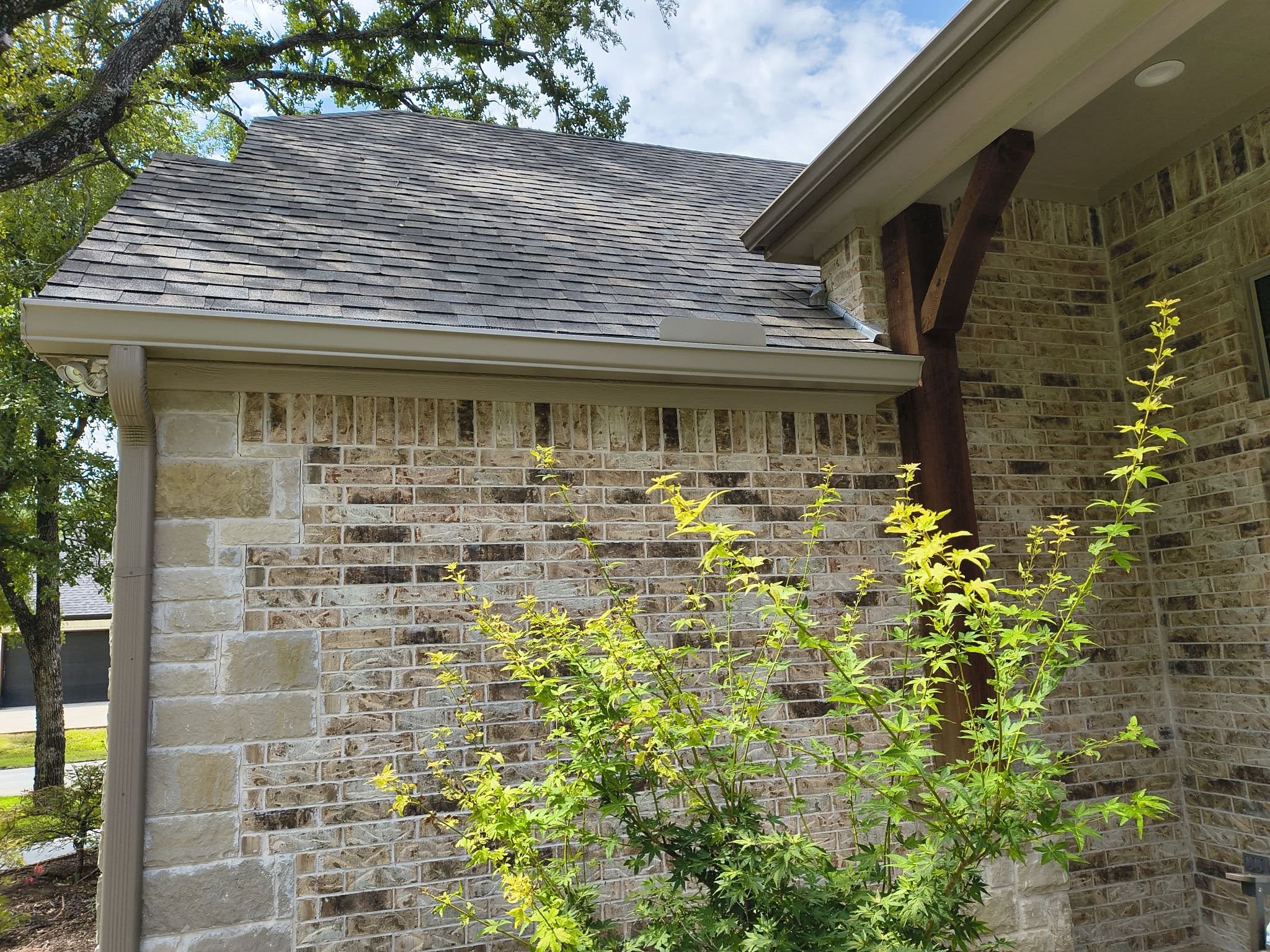 Light-colored gutter and downspout following the roofline of a brick home