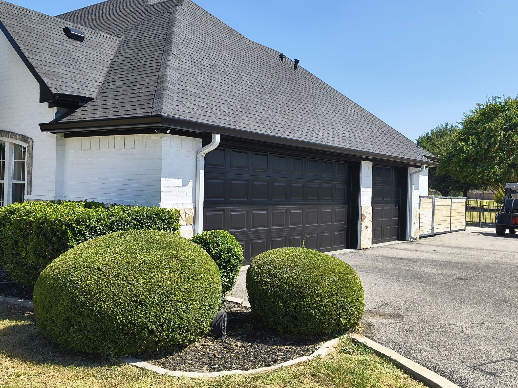Dark gutters along a garage roofline with white downspouts against white brick