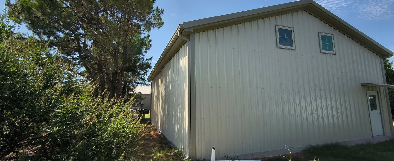 Light-colored metal building with a gutter along the side roofline and a corner downspout
