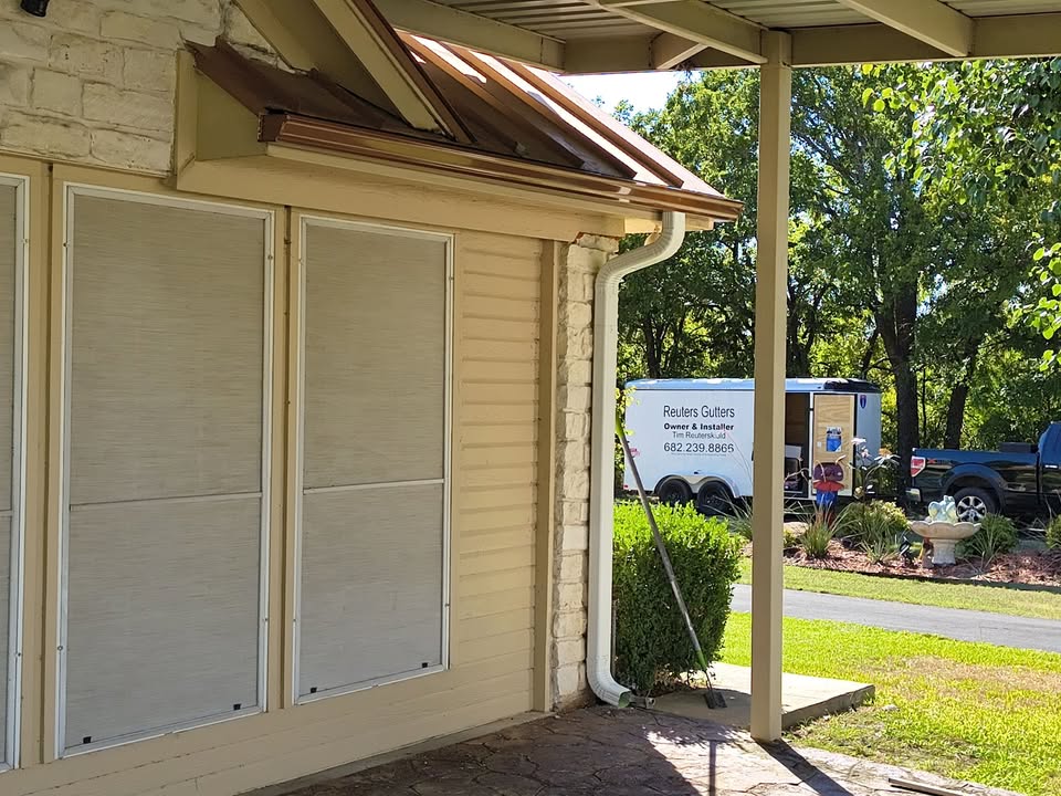 Gutter and downspout along a covered porch, with the Reuters Gutters trailer in the background